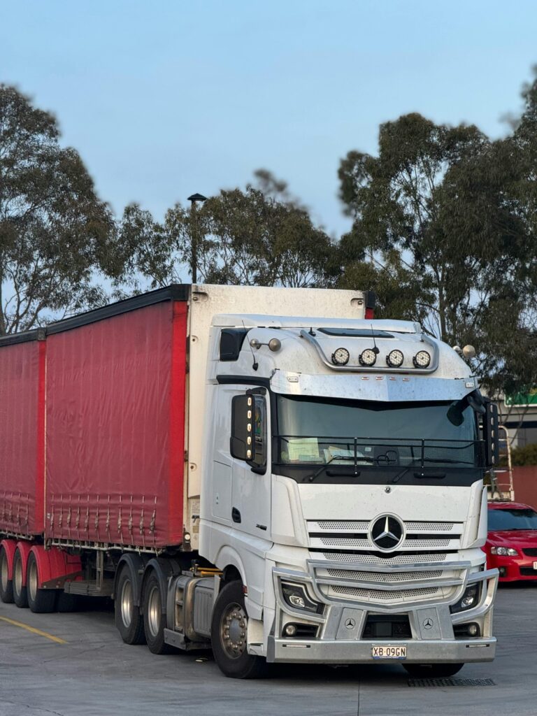 White and red semi truck parked outdoors at logistics hub, ready for transportation.